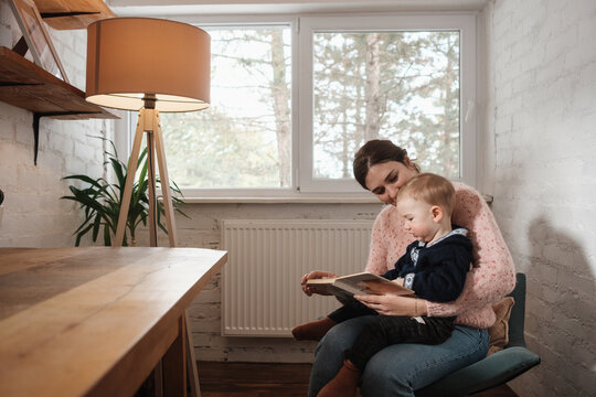Woman Reading A Book To A Baby In The Cozy Room