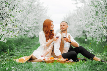 Picnic - Young couple in spring meadow. Alley of flowering cherry trees.