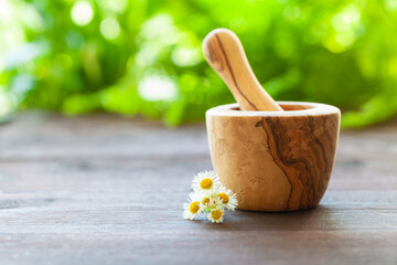 Homeopathic concept. A wooden mortar and pestle with calendula on a wooden table. A blurry green...