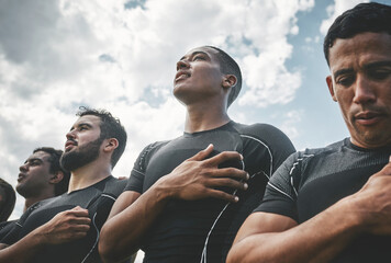 Standing proud. Cropped shot of a team of confident young rugby players standing at attention singing their anthem outside on a field before a rugby match. - obrazy, fototapety, plakaty