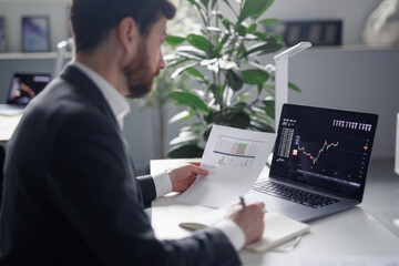 Male broker working with papers and checking trades