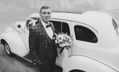 Handsome groom in plaid jacket and bow tie near white retro car