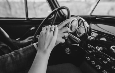 Newlyweds in a retro car hold hands behind the wheel and demonstrate wedding rings