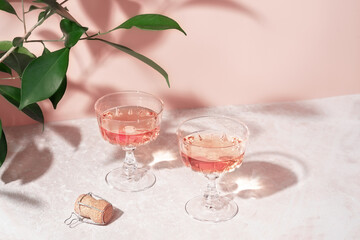 Two crystal glasses of rose sparkling wine or champagne on pastel pink marble table in sunlight. Minimal creative composition with copy space. Summer drink concept.