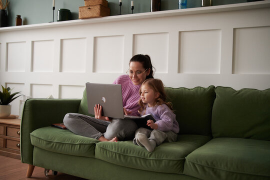 Mom working on laptop on couch, working from home, with daughter,