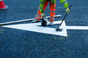 Obraz premium Roadworkers applying road marking on newly laid tarmac during new road construction