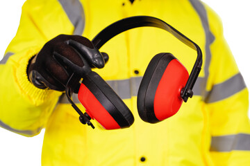 A construction worker in a hi-viz coat and black safety gloves giving ear defenders to viewers isolated on white background. Safety on construction site banner concept - obrazy, fototapety, plakaty