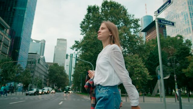 Millennial European Woman in White Shirt Crosses the Road Walking in City Downtown Streets in Frankfurt am Main, Germany at Daytime. Urban Lifestyle and Business concept. 4K low angle tracking shot