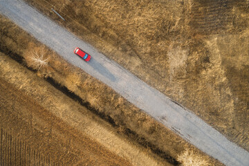 Aerial view of a rural road with low traffic. a lone red car is driving along the road. A power...