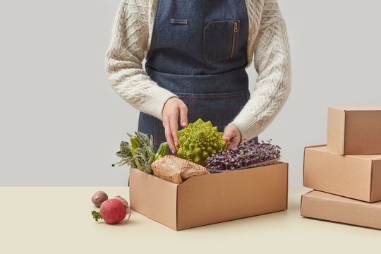Woman in apron packing fresh vegetables in box