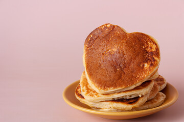 heart shaped pancakes lie in a yellow plate on a beige background, copy space, close up