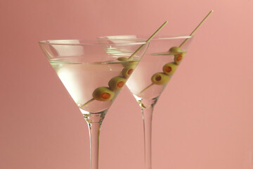two glasses of martinis with olives on a pink background