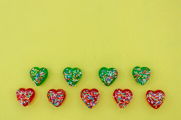 Flat lay red and green heart shaped jelly sweets with colorful sugar sprinkles on yellow background 