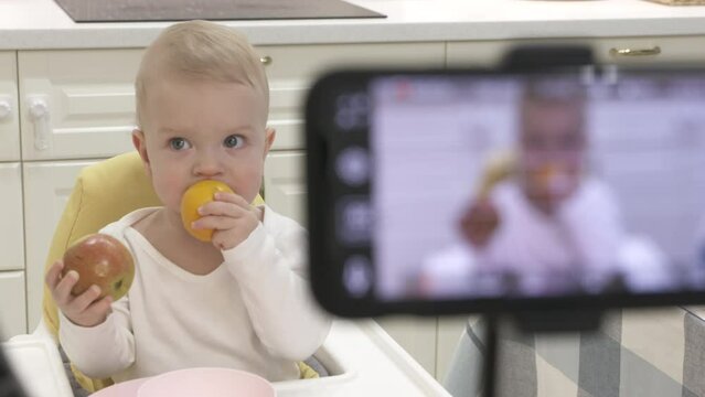 Recording video of kid on mobile phone with ring light, record photo video on smartphone of one-year-old baby boy with fruit. High quality 4k footage