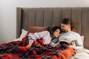 Couple reading book in bed under plaid
