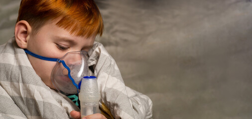 A young boy breathes through an inhaler in bed. Baby wrapped in a blanket. Treatment of bronchitis,...