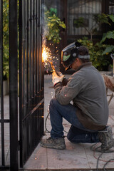 Fototapeta premium Welder welding a grating wearing a welder helmet with a beautiful welding flash 