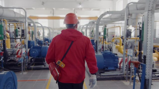 A man walks with his back in the premises of an oil plant. Modern equipment with a pipe or a powerful technological zone at an oil depot or tank farm. Extraction of rock oil for supplies. Engineering