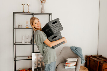 Attractive girl is packing the things. Young woman is holding the boxes and looking at the camera. The girl has an appealing and cute smile. Concept of moving