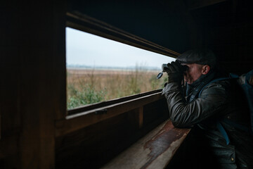 Man with binoculars in a wildlife hide.