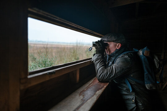 Man with binoculars in a wildlife hide.