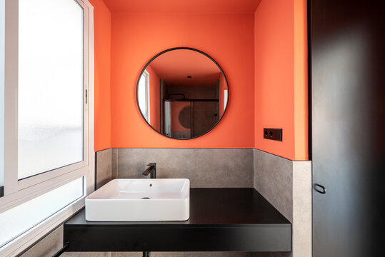 Bathroom With A White Porcelain Sink On A Black Wooden Countertop, A Walk-in Shower And A Round Mirror With A Black Frame To Match The Accessories Next To A White Aluminum Window