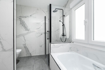 Bathroom with bathtub, individual shower cabin with black accessories and marble tiling on the walls - obrazy, fototapety, plakaty