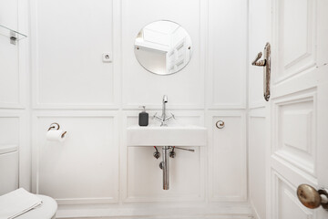 Hanging white porcelain sink on a white wooden wall with vintage faucet and round mirror
