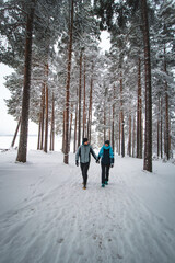 Fototapeta na wymiar Couple in love walking through a spruce forest in winter in Sotkamo, Finland. A man looks at his wife and they enjoy every moment together. Young couple hiking. Discovering Scandinavia