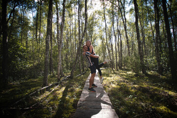 Obraz premium Couple in love hugging on duckboards in the middle of the Finnish wilderness. The joy of discovering Scandinavia. A girl looks down on her boyfriend. Real feelings in real life
