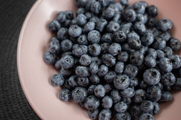 Blueberries in a pink plate on a gray table close-up.