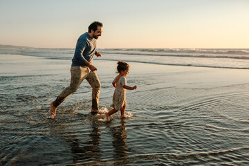 Fototapeta premium Father chasing daughter in ocean at sunset