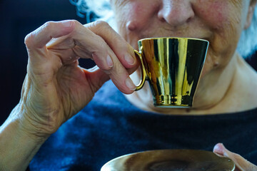 Old woman drinking Turkish coffee with golden colored cup, traditional Turkish coffee drinking...
