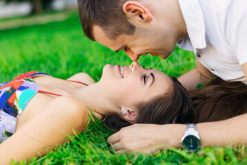 close-up of smiling young couple touching noses with closed eyes and lying on green grass.