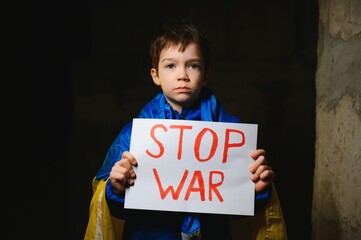 Portrait sad boy protesting war raises banner with inscription Stop War at blue yellow flag of country Ukraine. Call to stop war, child against war, crisis in Ukraine.