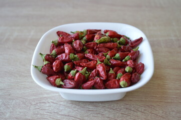 small extremely hot red peppers in a white bowl on a wooden table