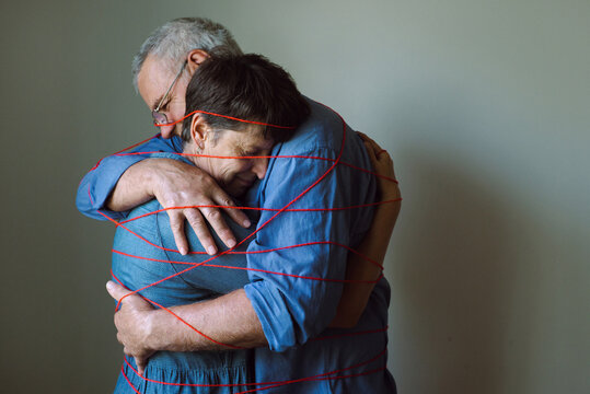 An elderly couple hugs and is tied with a red thread.