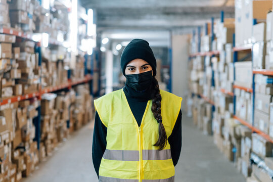Woman wearing mask standing between racks in warehouse