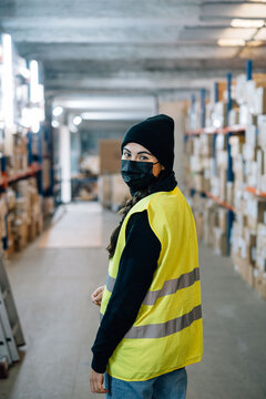 Woman wearing mask standing between racks in warehouse