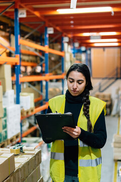 Young woman writing on clipboard in warehouse