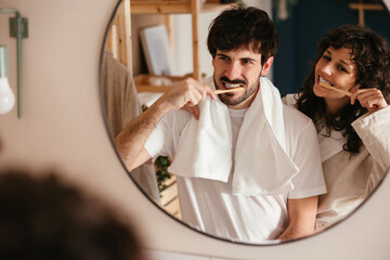 Smiling couple brushing teeth in bathroom