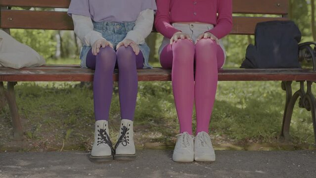 Bright tights on the legs of teenage girls sitting on a park bench.
