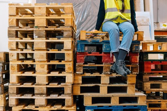 Employee sitting on heap of pallets in warehouse