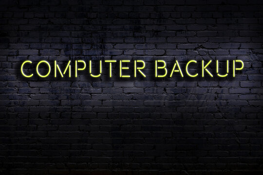 Night view of neon sign on brick wall with inscription computer backup