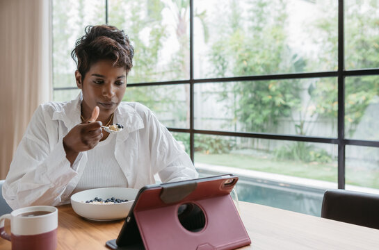 Young woman eating breakfast while reading a tablet