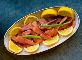 Dish with cold smoked salmon slices decorated with lemon and green onion