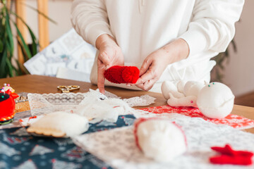 Female hands make handmade dolls on the background of multicolored fabric, scissors. Close up. A woman sews clothes for a doll.
