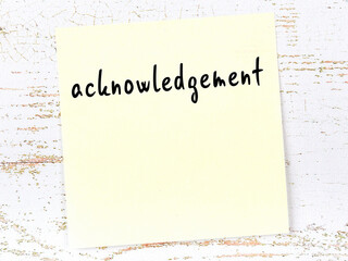 Yellow sticky note on wooden wall with handwritten word acknowledgement