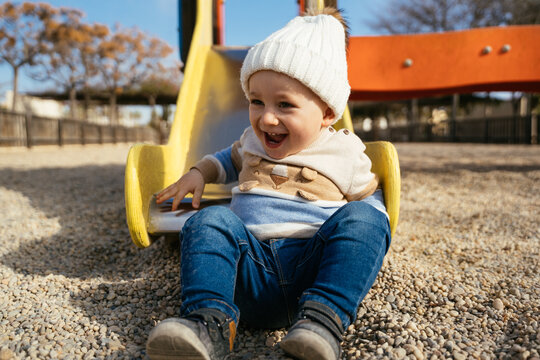Laughing boy in warm clothes sitting on slide