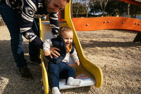 Father giving slide ride to little son on playground